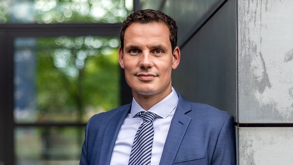 Prof. Dr. Dr. Erik Hahn steht an eine graue Mauer gelehnt und lächelt in die Kamera.