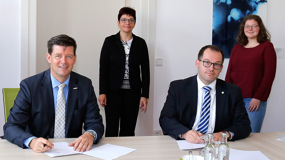 Frank Kebbekus und Prof. Dr. Alexander Kratzsch im Vordergrund bei der Vertragsunterzeichnung. Im Hintergrund Kanzlerin Karin Hollstein und Studentin Nicola Bell.