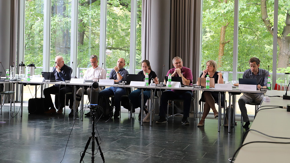 Senatsmitglieder sitzen am Tisch in der Aula.