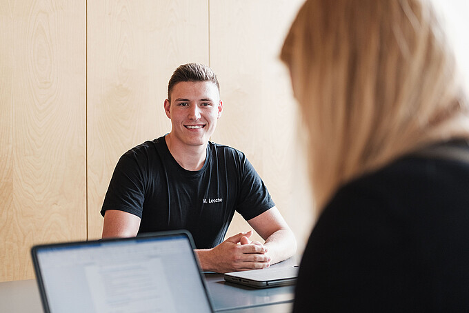 Ein KIA-Student unterhält sich sitzend an einem Tisch mit einer blonden Frau.