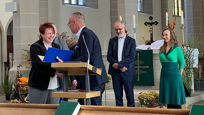 In einer Kirche am Altar freut sich Cornelia Müller über das Stipendium aus den Händen des Vorsitzenden des Stiftungsrates, Dr. Uwe Koch.