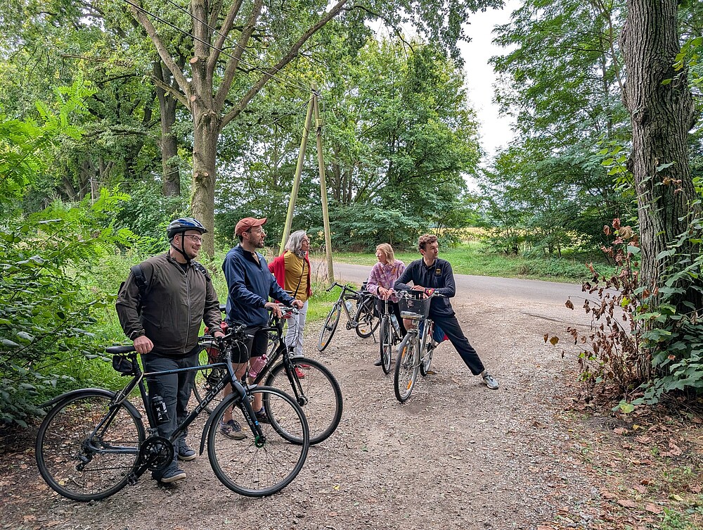 5 Menschen stehen mit ihren Fahrrädern zwischen Bäumen im Grünen