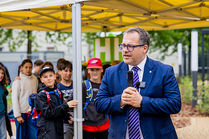 Der Rektor hält eine Ansprache neben Schülern.