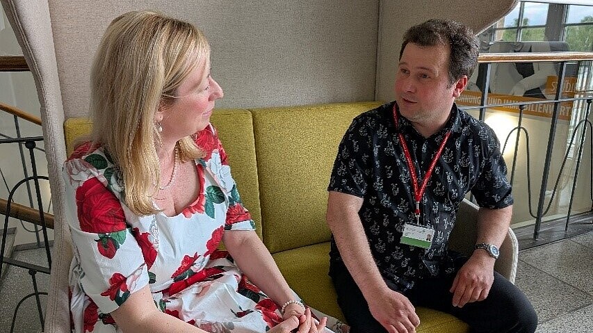 Sophia Keil und Nikolay Belov sitzen auf einem hellgrünen Sofa und unterhalten sich.
