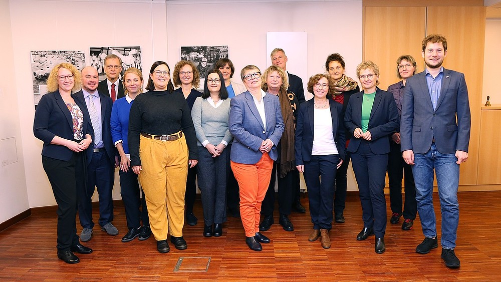 Vertreterinnen und Vertreter unter anderem vom Bündnis der Kommunalen Gleichstellungsbeauftragten der Lausitz stehen für ein Gruppenbild in einem Raum vor einer Wand mit schwarz-weiß Bildern und lächeln in die Kamera.