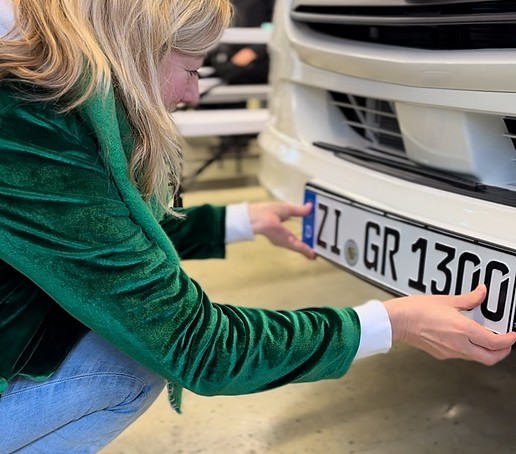 Die Prorektorin bringt das Kfz-Kennzeichen an den Sprinter an.