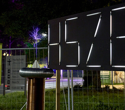 Das HSZG-Logo leuchtet hell, im Vordergrund ist ein lila Blitz zu sehen.