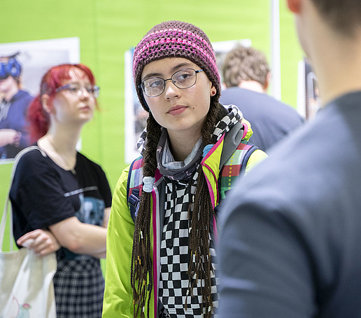 Eine Besucherin mit Strickmütze schaut sich am HSZG-Stand um.