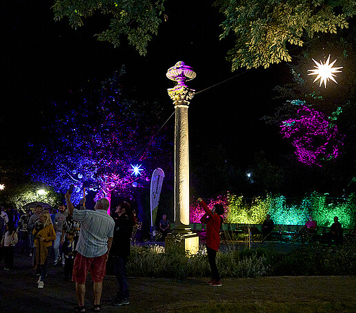 Eine bunt angestrahlte Parkanlage mit Besuchern.