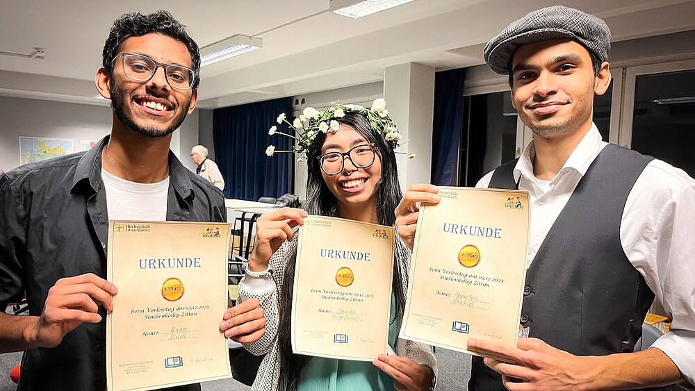 Der Gewinner und die beiden Zweitplatzierten halten ihre Urkunden in die Kamera.