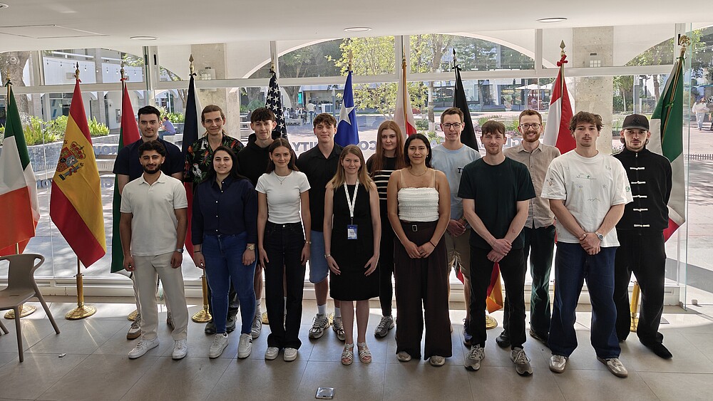Prof. Dr.-Ing. Patricia Stang (1. Reihe, 4.v.l.) von der Fakultät Elektrotechnik und Informatik mit Studierenden am Tecnológico de Monterrey stehen im Foyer eines Gebäudes vor Glasfenstern nebeneinander zum Gruppenfoto.