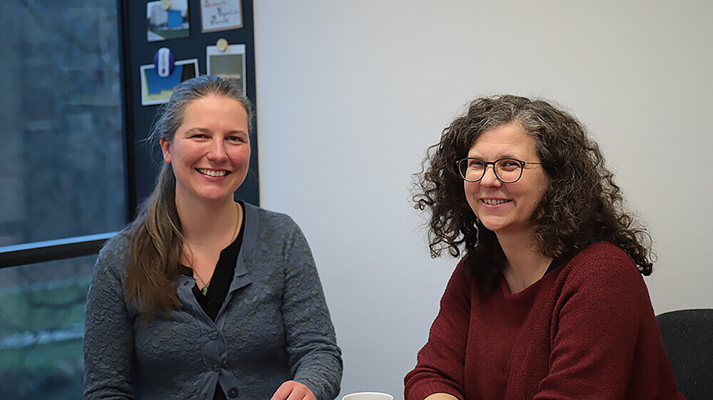 Sabine Bublitz und Professorin Schulze sitzen am Tisch und lächeln in die Kamera.
