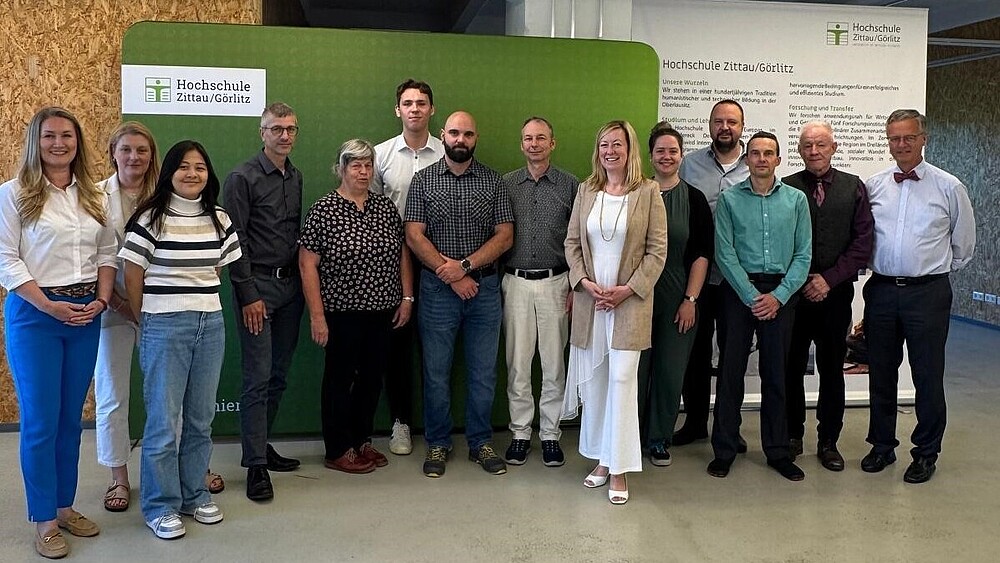 Vertretende der HSZG und Infineon Technologies stehen im Celsiuz zum Gruppenbild nebeneinander vor einer grünen Pressewand und einem HSZG-Rollup.