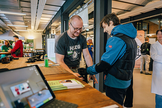 ein Mitarbeiter legt einem Besucher den Alters-Simulationsanzug an 