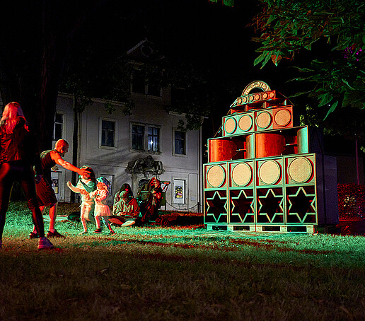 Ein Kunstobjekt auf einer Wiese, Kinder laufen einem Mann in die Arme.