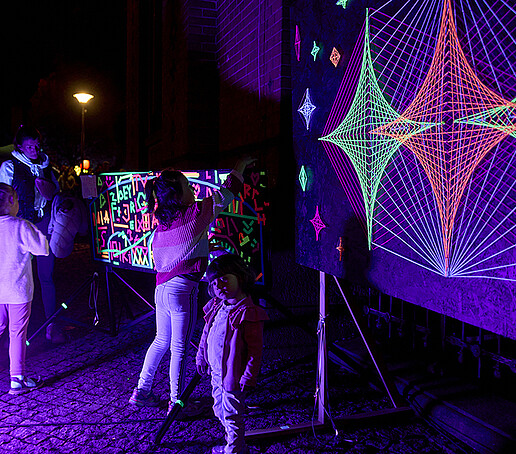 Kinder malen mit Neonfarben auf einer Leinwand.