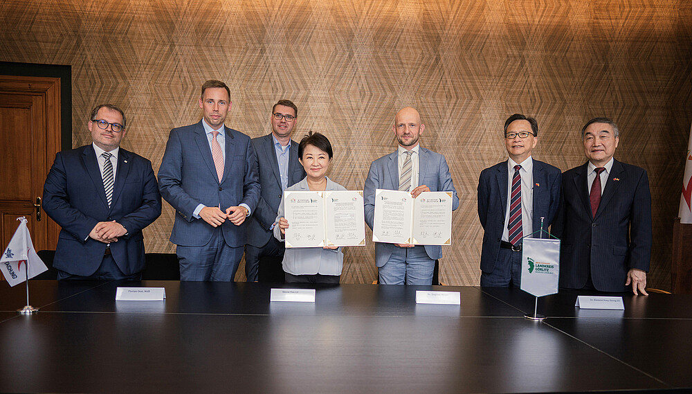 Vertretende aus dem Landkreis Görlitz, Taiwan und der HSZG stehen in einem Sitzungssaal nebeneinander und lächeln in die Kamera, der Landrat und die taiwanesische Vertretung halten das unterzeichnete Memorandum vor sich in die Kamera.
