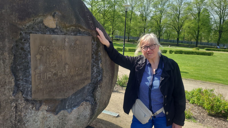 Mrs. Schönfelder is standing in a park and leaning against a large stone.