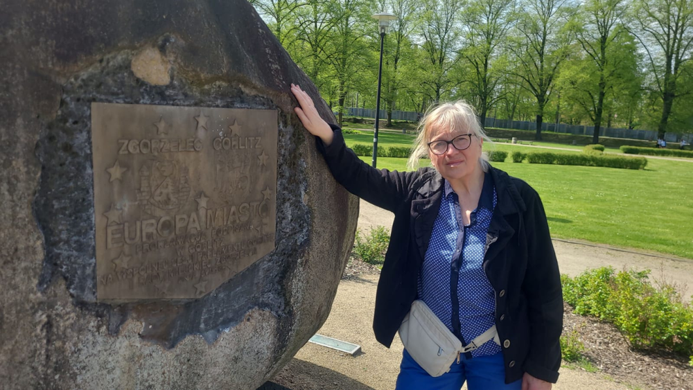 Mrs. Schönfelder is standing in a park and leaning against a large stone.