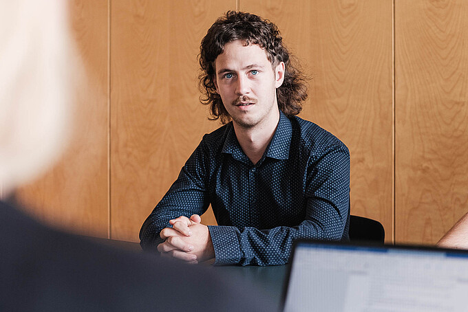 Ein KIA-Student sitzt bei einer Besprechung an einem Tisch.