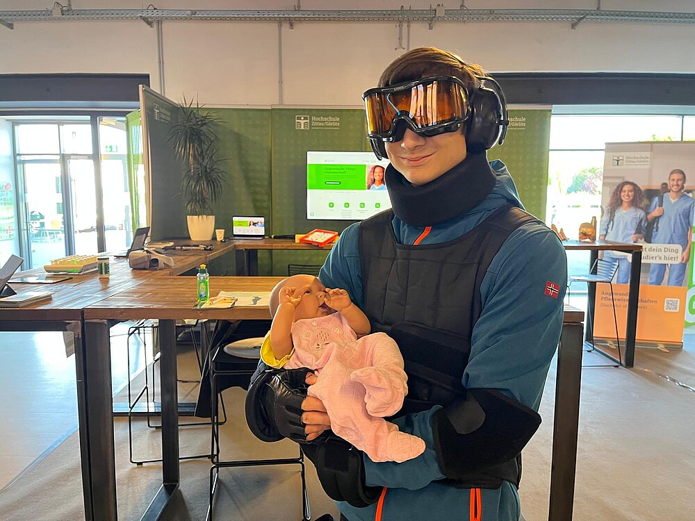 junge Frau in einem Alters-Simulationsanzug mit einer Baby-Atrappe auf dem Arm