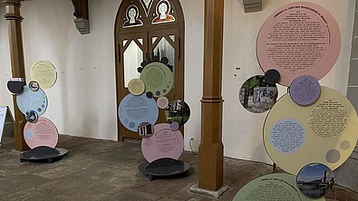 In einer Kirche sind rund ausgeschnittene Ausstellungsstücke zu sehen. Eine Kirchentür im Hintergrund.