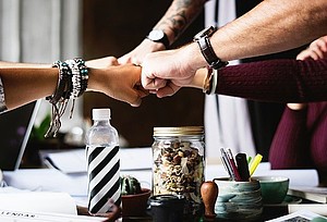 Symbolbild Teamarbeit (Quelle: Pixabay) Hände mehrerer Personen berühren sich über einem Tisch